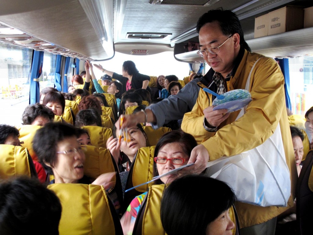 聯盟副主席盧偉國在旅遊車上向街坊派發印有經民聯會徽的紀念品圓扇，並解釋扇上聯盟會徽的意義。他說：「經民聯會徽象徵我們會凝聚各界力量，憑藉朝氣和動力，推動社會發展。」