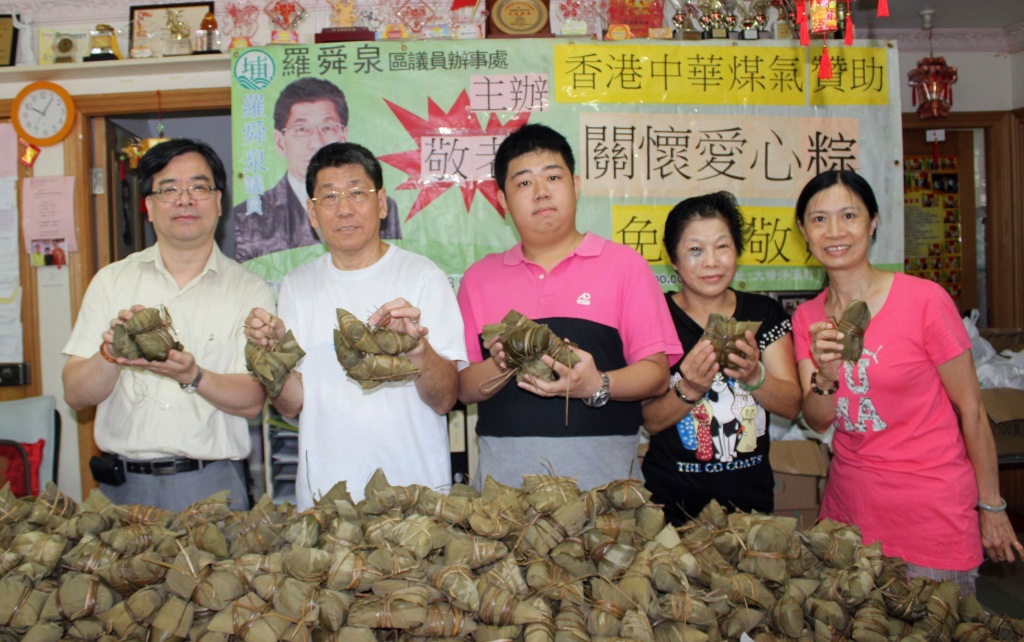 大埔區區議員羅舜泉(左二)、地區發展幹事周秉謙(中)於大埔泮涌村向長者派發1500多隻愛心糭。羅舜泉說：「因爐具所限，每次烚糉只可以放約300隻，我們花了一整晚通宵製作糭子，十分感謝義工們的協助。」